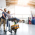 Je crois que je peux voler. Une femme rayonnante est assise sur un bagage et un homme tire un chariot. Ils regardent devant eux avec un sourire radieux. Espace réservé à droite